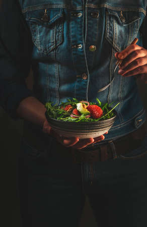 Healthy vegan lunch. Woman in blue denim holds ceramic bowl with avocado, arugula, grapefruit and cashew salad in her hands. Comfort, clean, vegetarian diet food conceptの写真素材