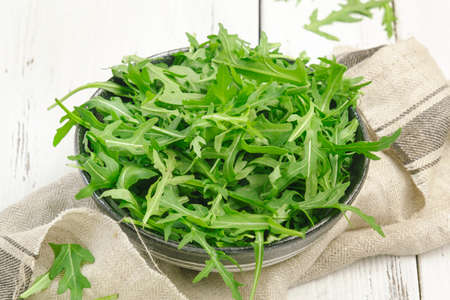 Fresh green arugula in rustic ceramic bowl on white kitchen table background, top view, copy space....