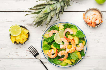 Pineapple shrimp salad with spinach, avocado and lime on white wooden kitchen table, top view. Healthy eating, balanced, clean diet food, weight loss conceptの写真素材