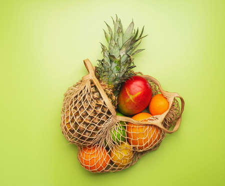 Eco friendly shopping bag with various tropical fruits on green background. Pineapple, mango, kiwi,...