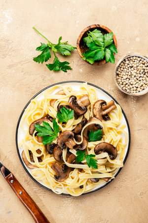 Delicious pasta with champignon mushrooms on plate with parsley on beige stone kitchen table background, top view. Healthy vegan cooking and eating. Italian food conceptの写真素材