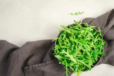 Fresh green arugula in ceramic bowl on gray kitchen table, top view, copy space. Spring spicy herb for healthy diet eatingの写真素材