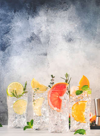 Gin tonic citrus cocktails set. Alcoholic drinks with lime, lemon, grapefruit, orange, soda and herbs in highball glasses, gray background. summer cocktail partyの写真素材