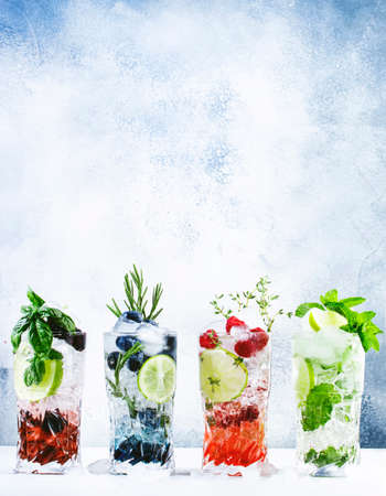Summer cocktails or mocktails and cold drinks. Refreshing mojito drink with blueberries, blackberries, raspberries and lime, herbs and ice on gray backgroundの写真素材