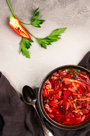 Homemade red cabbage soup with beets, vegetables and herbs, Russian borscht in plate on gray kitchen...