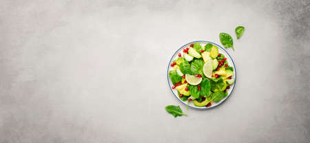 Vegan vegetarian salad with pineapple, spinach, avocado and pomegranate, gray stone kitchen table,...