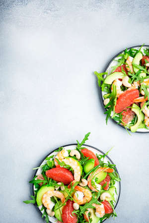 Fresh summer salad with shrimps, avocado, pink grapefruit, arugula and cashews. Gray stone kitchen table background, top view, copy spaceの写真素材