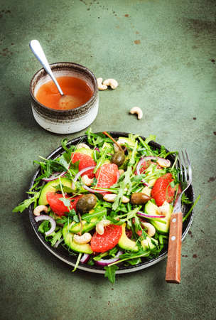 Healthy vegan salad with arugula, avocado, juicy grapefruit, cashews and dressing with olive oil,...