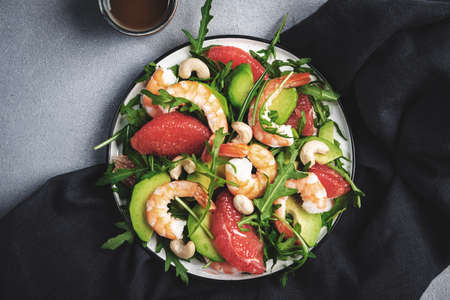Fresh summer salad with shrimps, avocado, pink grapefruit, arugula and cashews. Gray stone kitchen table background, top view, copy spaceの写真素材