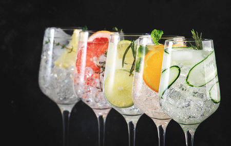 Gin tonic cocktails set in wine glasses. Trendy Alcoholic drinks with lime, lemon, grapefruit, orange, cucumber, soda and spicy herbs, black background. summer cocktail partyの写真素材