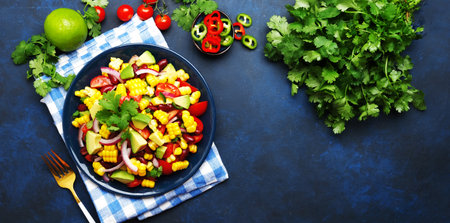 Mexican spicy salad with corn, red beans, avocado, jalapeno peppers, cherry tomatoes, onion and cilantro. Blue table background, top viewの写真素材