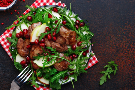 Healthy fresh chicken liver salad with apple, pomegranate and arugula. Brown kitchen table background, top view, copy spaceの写真素材