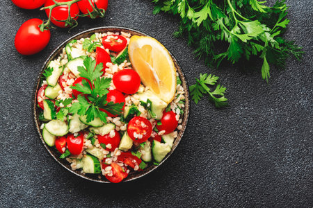 Bulgur tabbouleh salad with fresh tomatoes, cucumbers, parsley and lemon dressing. Traditional Middle Eastern and Arabic dish. Black stone kitchen table background, top viewの写真素材