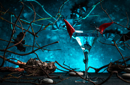 Halloween alcoholic cocktail evil martini on scary dark blue background with twisted branches, bats, stones and spiders, festive drink with horns for partyの写真素材