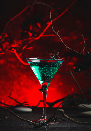 Halloween witch potion alcoholic cocktail on scary dark red background with twisted branches, bats, stones and spiders, festive drink for partyの写真素材