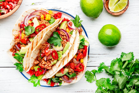 mexican cuisine. Tacos with beef, corn, red beans, tomato salsa sauce and onions in corn tortilla on plate. White table background, top viewの写真素材