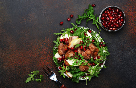 Healthy fresh chicken liver salad with apple, pomegranate and arugula. Brown kitchen table background, top view, copy spaceの写真素材