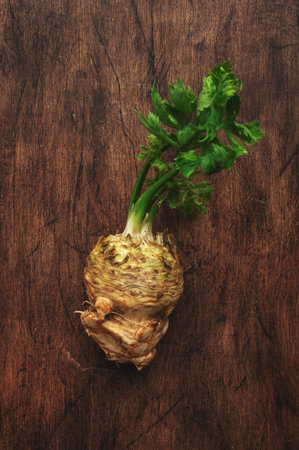 Root celery with green stems, rustic wooden kitchen table background, top view