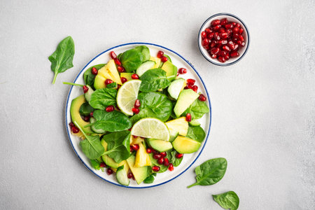 Fresh vegan salad with pineapple, spinach, avocado and pomegranate seeds, gray kitchen table, top view. Healthy eating, clean food, diet, weight loss conceptの写真素材