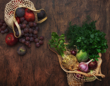 Autumn food background with vegetables, root crops and fruits in string bag: celery, carrots, apples, pomegranate, figs, grapes. Harvesting, local farm market shopping, healthy eating concept. top viewの写真素材