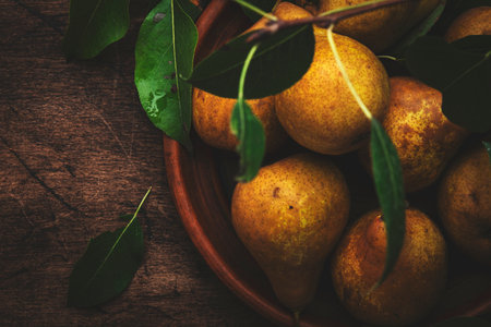 Autumn harvest of yellow pears with leaves on clay plate on old rustic wood kitchen table backgroundの写真素材