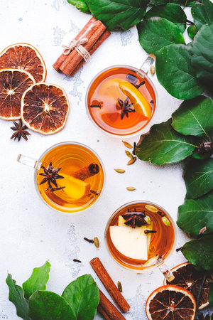 Mulled Cider glass cups: apple, pear and orange flavored hot cider with spices. Fermented low alcohol cocktail fruit drink on white table with leaves, top viewの写真素材