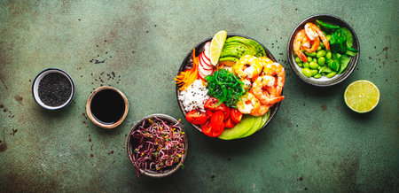 Hawaiian poke bowl with shrimp, avocado, radish, carrot, tomato, chuka seaweed and white rice. Soy sauce, lime and sesame dressing. Green table background, top view bannerの写真素材