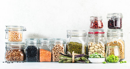 Legumes and beans. Dried, raw and fresh. Lentils, chickpeas, mung beans, soybeans, edamame, peas in glass jars. Healthy diet food, vegan protein, micronutrients and fiber sources. White kitchen. Bannerの写真素材