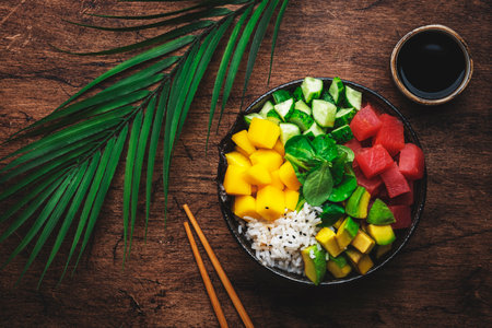 Hawaiian poke bowl. Trendy dish with tuna, avocado, mango, cucumber, lamb lettuce and white rice. Soy sauce, lime and sesame dressing. Old wood table background, top viewの写真素材