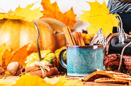 Autumn hot drink in white cup on fall background with pumpkins, spices, fallen leaves, autumn clothes, scarves on rustic wood table, copy spaceの写真素材