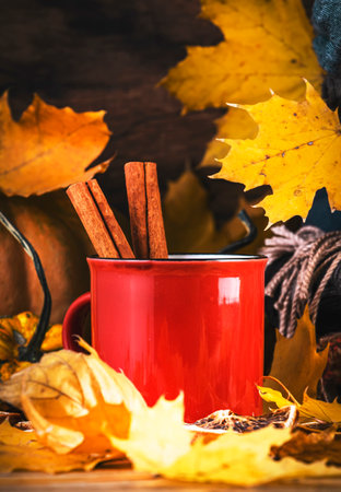Autumn hot drink in red cup on fall background with pumpkins, fallen leaves, autumn clothes, scarves on rustic wood tableの写真素材