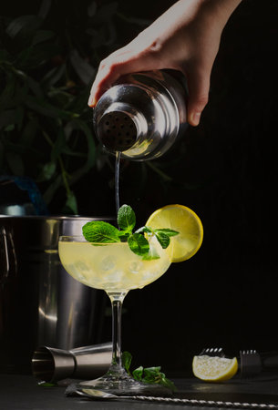 White lady alcoholic cocktail with dry gin, liquor, lemon juice and ice in glass. Bartender pours cocktail from shaker into glass. black backgroundの写真素材