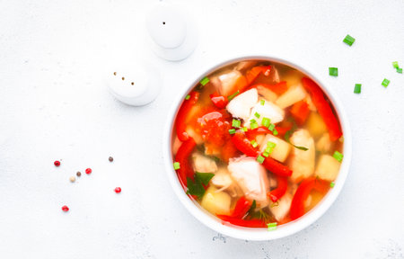 Fish soup with trout, red paprika, potatoes, tomatoes and parsley in ceramic soup bowl on white table background, top viewの写真素材
