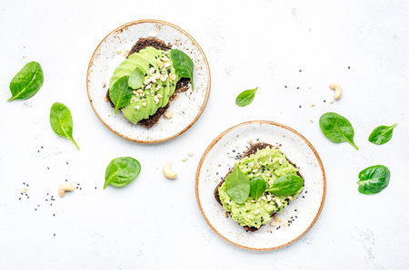 Avocado sandwich or toast on rye bread with spinach, crushed cashew nuts and sesame seeds, on plate,...