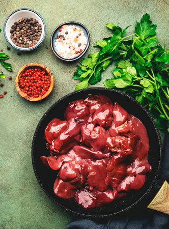 Fresh raw chicken liver in frying pan and ingredients for cooking on concrete green kitchen table, top view, copy spaceの写真素材