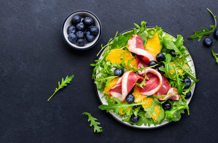 Delicious salad with smoked duck, oranges, blueberries, arugula and lettuce, black table background, top viewの写真素材