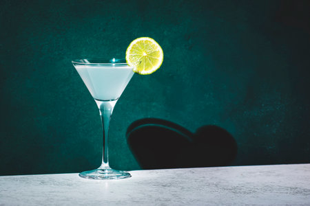Vodka gimlet alcoholic cocktail drink with vodka, syrup, lime juice and ice, dark green background, bright hard light and shadow patternの写真素材