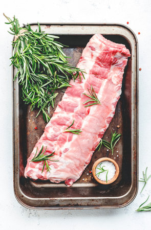 Raw pork ribs with rosemary and spices on the baking sheet, prepared for cooking on white kitchen table background, top viewの写真素材