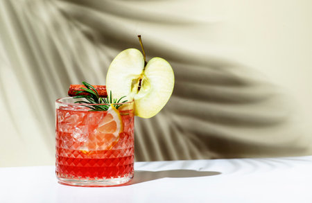 Apple pie alcoholic cocktail drink with vodka, apple liqueur, cinnamon, lemon, garnished with rosemary. Light beige background, hard light, shadow patternの写真素材