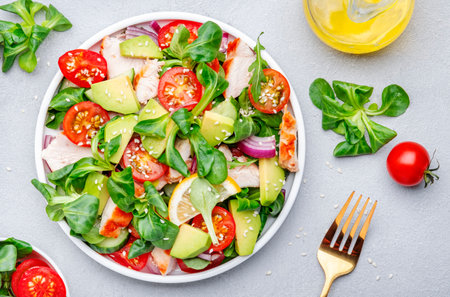 Chicken salad with red tomato, avocado, cucumber, red onion, lamb lettuce and sesame seeds on gray table background, top viewの写真素材