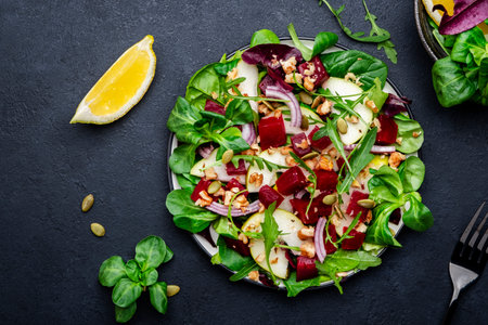 Beet and pear healthy salad with arugula, lamb lettuce, red onion, chard and walnut, black kitchen table. Fresh delicious vegan dish for healthy eatingの写真素材