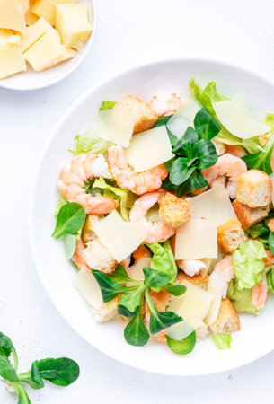 Caesar salad with shrimp, iceberg and lamb lettuce, croutons, parmesan cheese with caesar dressing. White table background, top viewの写真素材