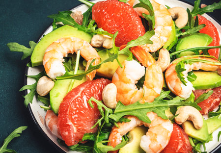 Seafood salad with shrimps, avocado, grapefruit, arugula and cashews. Dark kitchen table background, top view, close-upの写真素材