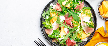 Delicious melon salad with cantaloupe, prosciutto, soft cheese and arugula on white table background, top viewの写真素材