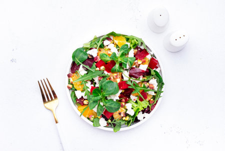 Beet, cheese and orange healthy salad with arugula, lamb lettuce, mini chard and pistachios, white kitchen table, copy space.. Fresh useful dish for healthy eatingの写真素材