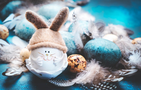 Easter rabbit with blue painted eggs, spotted feathers on blue background in festive Easter compositionの写真素材