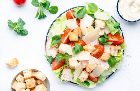 Caesar salad with chicken, iceberg salad, croutons, parmesan cheese and tomatoes with caesar dressing. White table background, top viewの写真素材