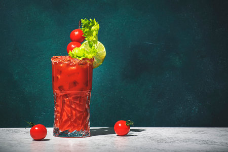 Bloody Mary classic alcoholic cocktail drink with tomato juice, vodka, lemon, celery, hot sauce and ice in glass garnished with salt and chili pepper. Green background, hard lightの写真素材