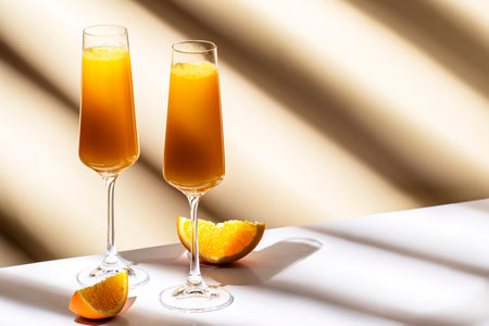 Mimosa alcohol cocktail drink with orange juice and cold dry champagne or sparkling wine in glasses. Beige background, hard light, shadow patternの写真素材