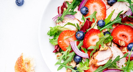 Strawberry, grilled chicken fillet and herbs healthy salad with arugula, blueberries and walnuts, white kitchen table, place for text. Fresh useful dish for eating healthyの写真素材